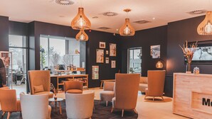 Een moderne lobby met verschillende zithoeken, een receptiebalie en decoratieve verlichting.