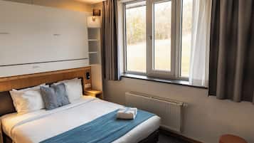 Une chambre d’hôtel avec un lit, une fenêtre avec des rideaux, un radiateur et une armoire.