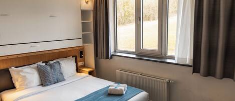 A hotel room with a bed, a window with curtains, a radiator, and a wardrobe.