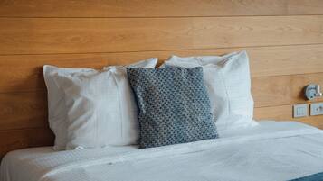 Een hotelkamer met een houten hoofdbord, een bed met witte en gemêleerde kussens, een donkerblauwe sprei en een opgerolde handdoek op het bed.