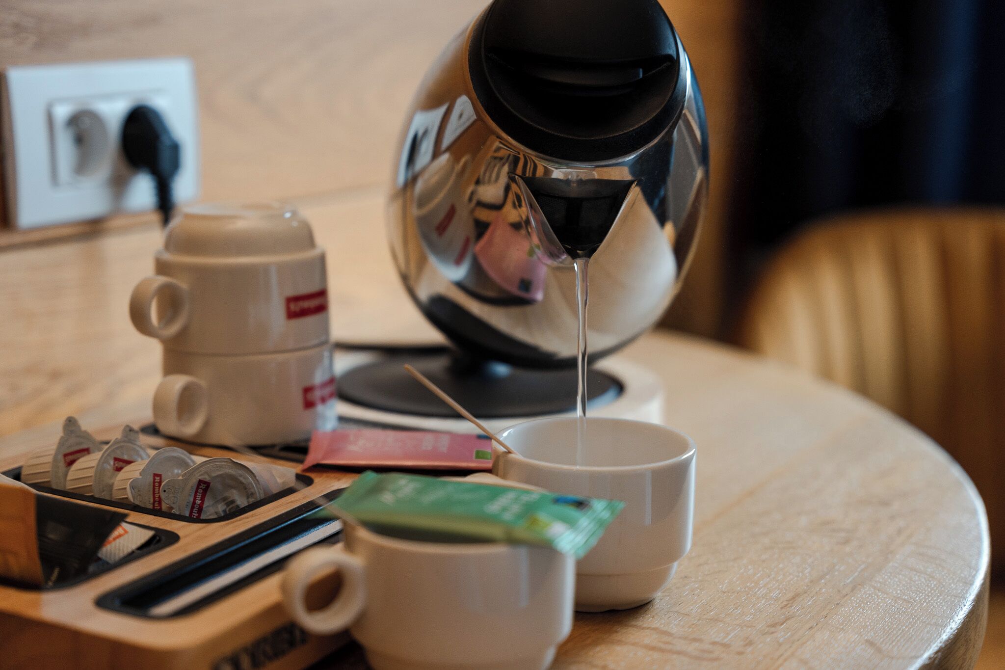 A coffee maker, a cup, and a teapot on a wooden table.