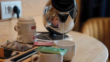 A coffee maker, a cup, and a teapot on a wooden table.