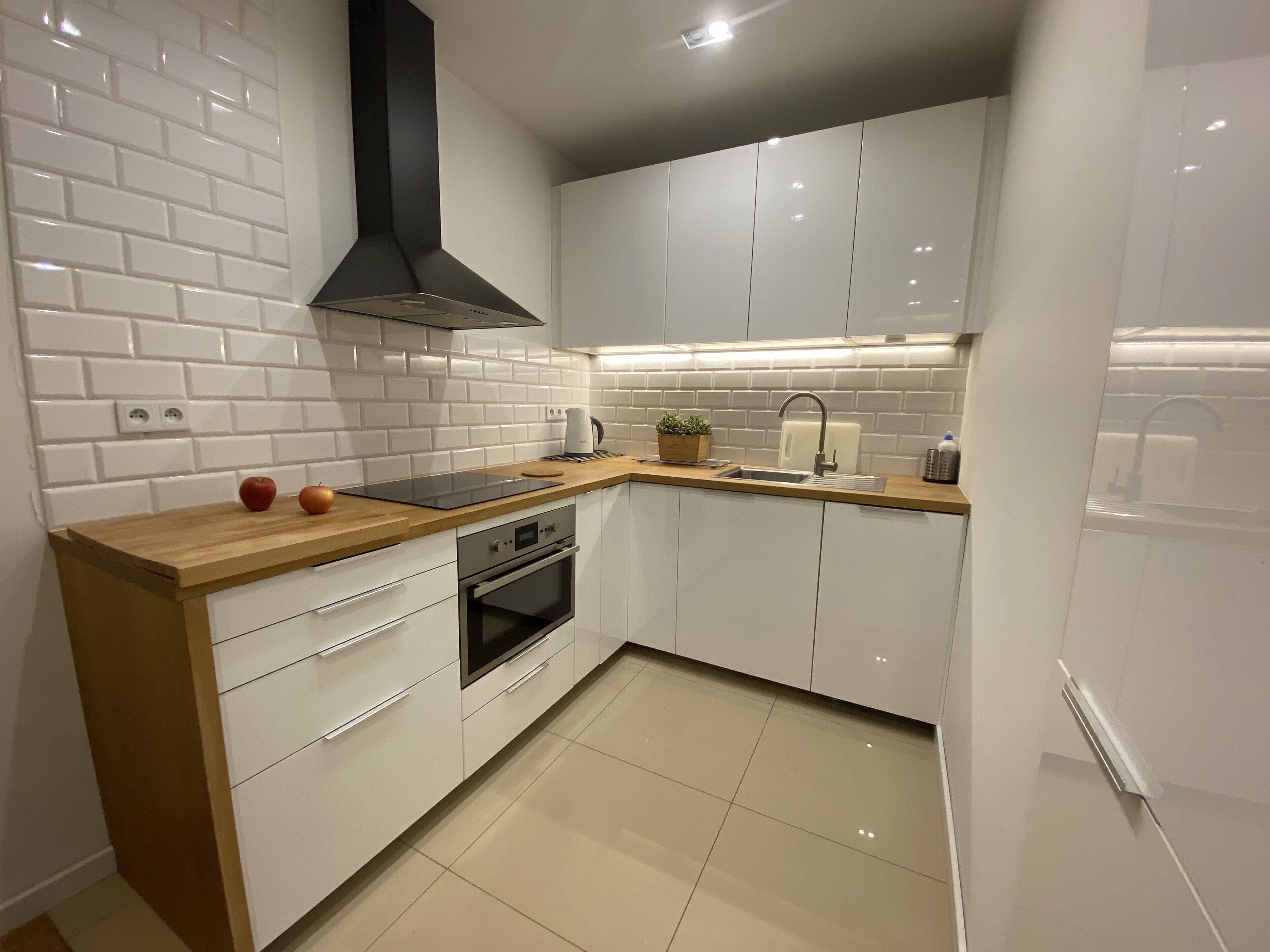Een moderne keuken met witte kasten, een zwarte afzuigkap, een inbouwoven en een roestvrijstalen spoelbak.