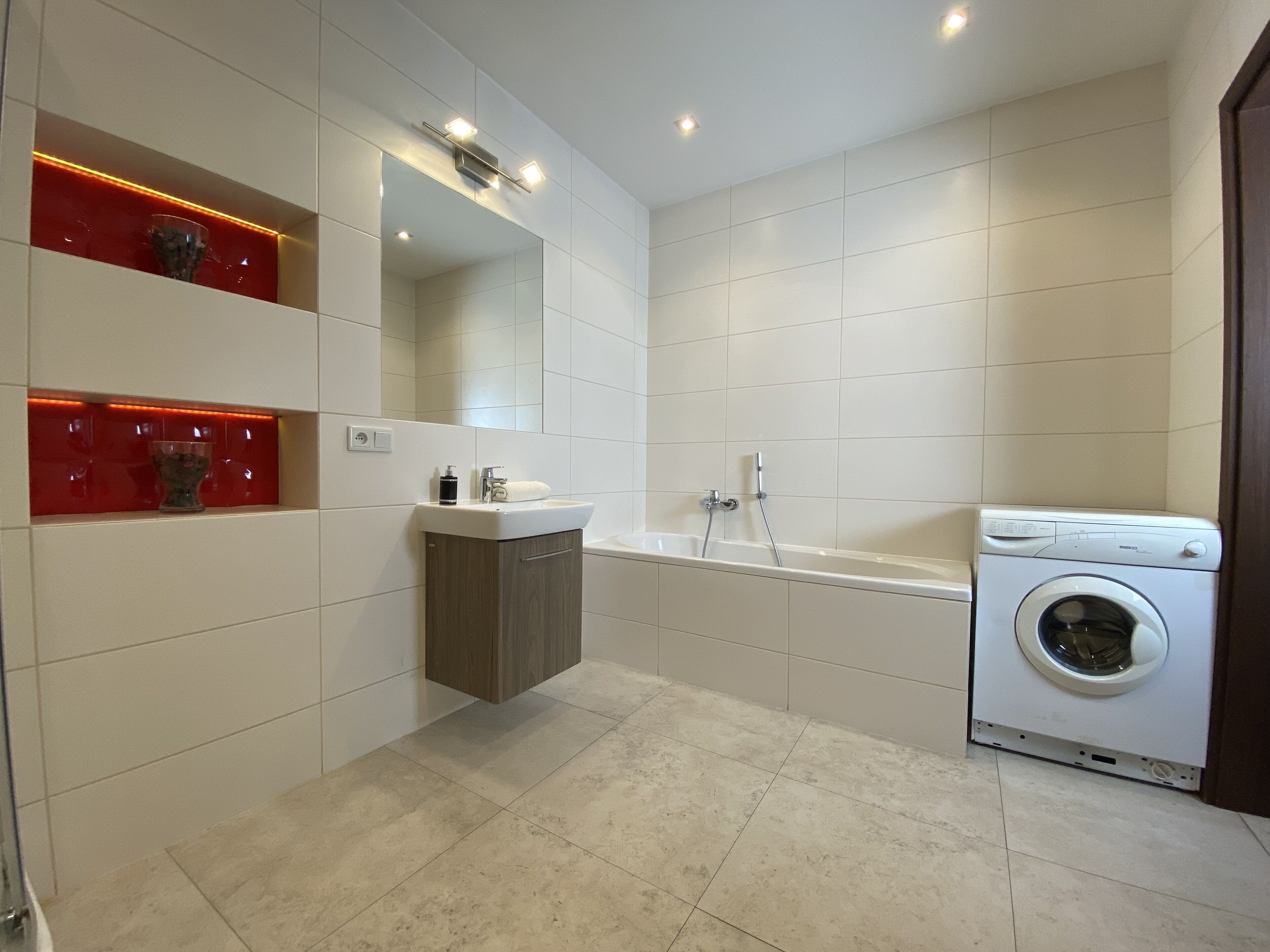 Un baño moderno con lavamanos, espejo, tocador, bañera y lavadora.