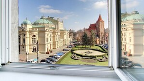 A view of a historic building complex with ornate architecture, a central tower, and a circular garden with a tree. - P&J Apartments (Kraków)
