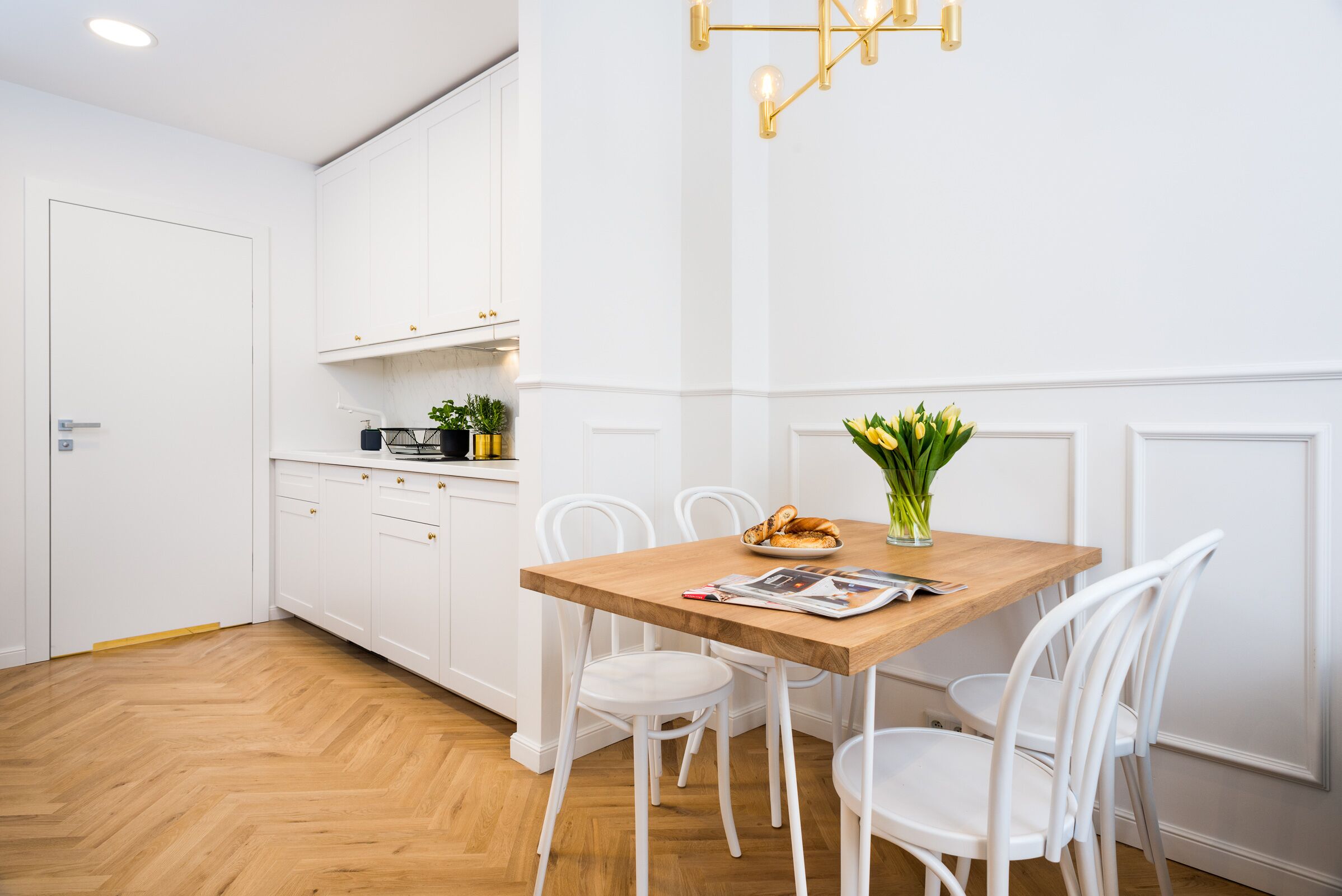 Una cocina moderna con armarios blancos, una mesa de comedor de madera y sillas blancas.