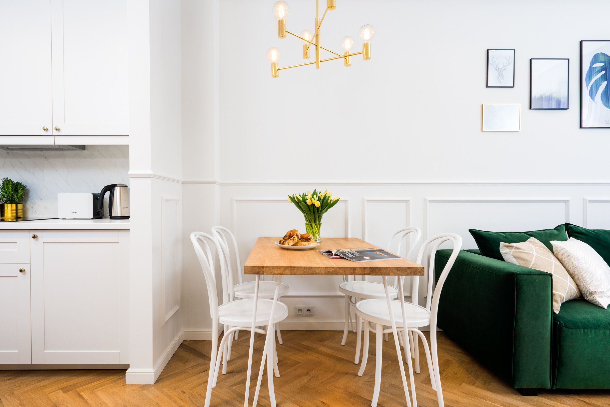 Une cuisine moderne avec des meubles blancs, une table à manger en bois et un canapé vert.