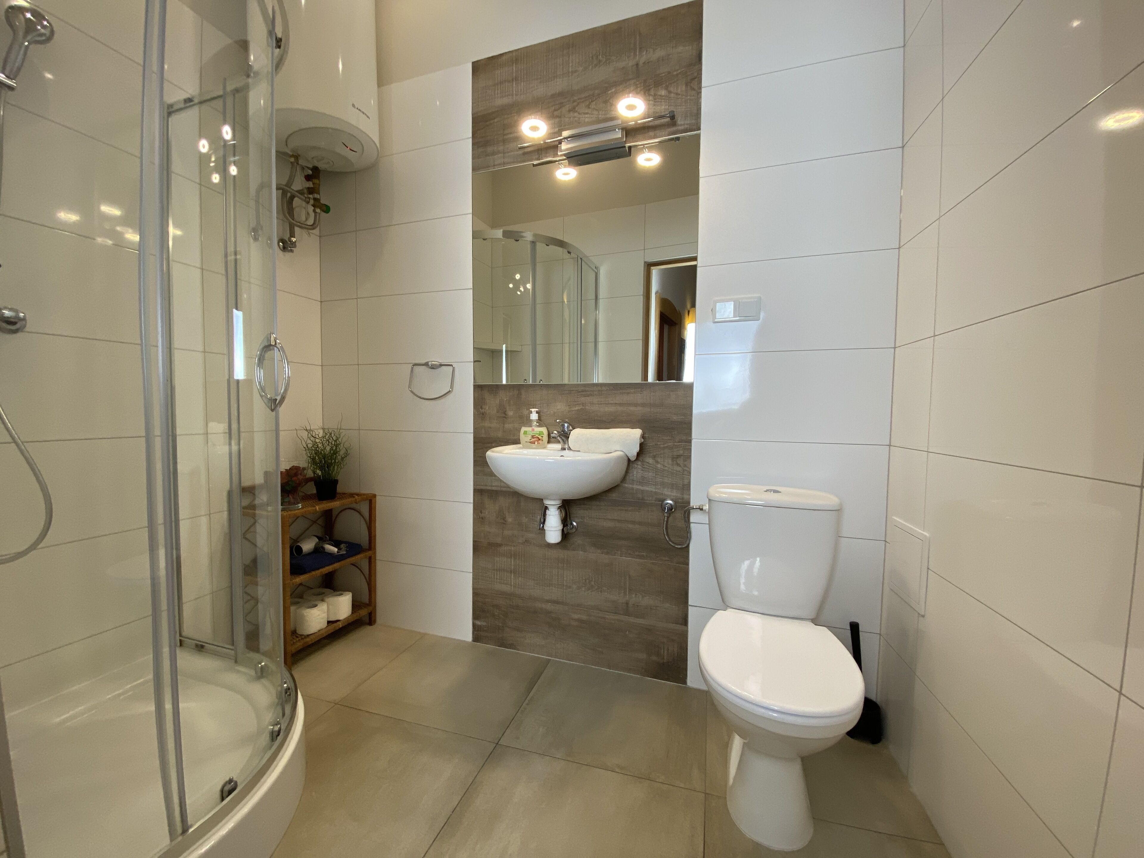 Een moderne badkamer met een douchecabine van glas, een houten plank met toiletartikelen, een wastafel en een toilet.