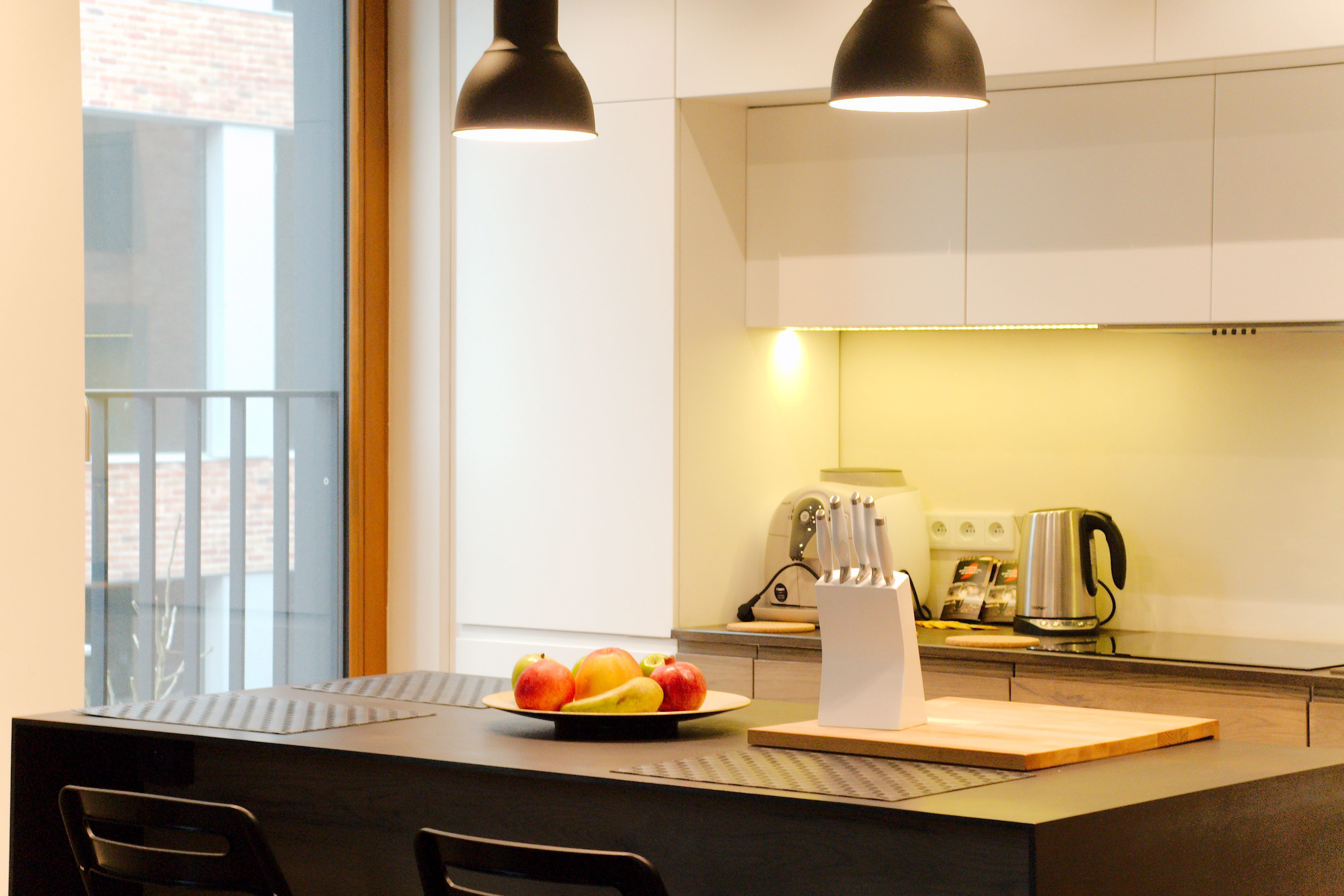 A modern kitchen with a dining area, featuring a fruit bowl, a kettle, and a knife block.