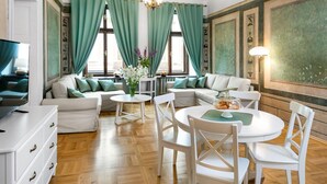 A modern living room with a sofa set, a dining table with chairs, and a television on a cabinet. - P&J Apartments (Kraków)
