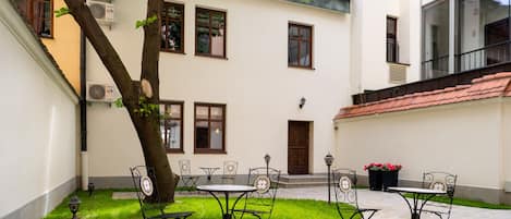 A courtyard with a stone patio, metal chairs, a table, and a tree.