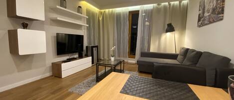 Una sala de estar moderna con un televisor de pantalla plana, estanterías empotradas, un sofá gris y una mesa de centro de madera.