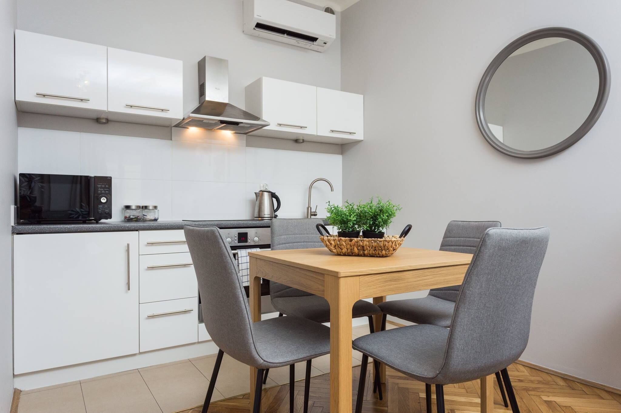 Una cocina moderna con armarios blancos, microondas, hervidor y una mesa de comedor con cuatro sillas.