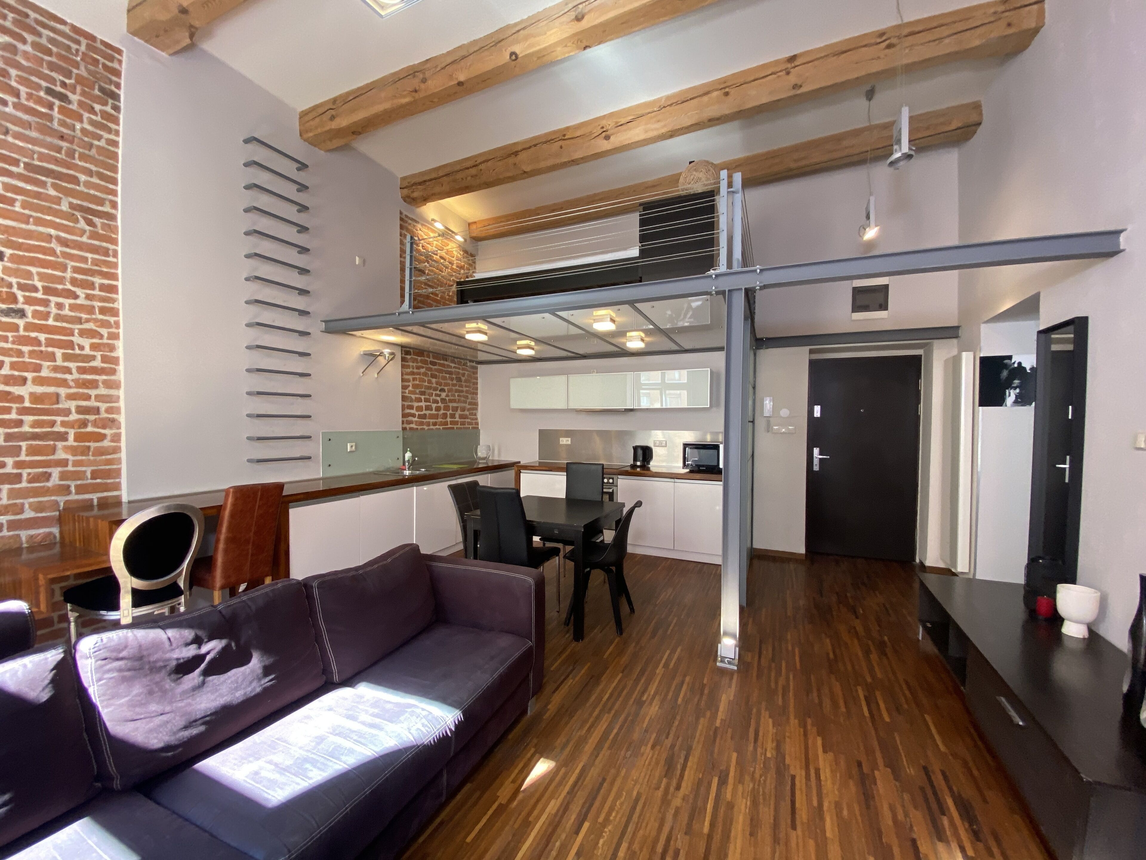 Un espacio habitable moderno con techo de madera, pared de ladrillo, sofá, mesa de comedor y zona de cocina.