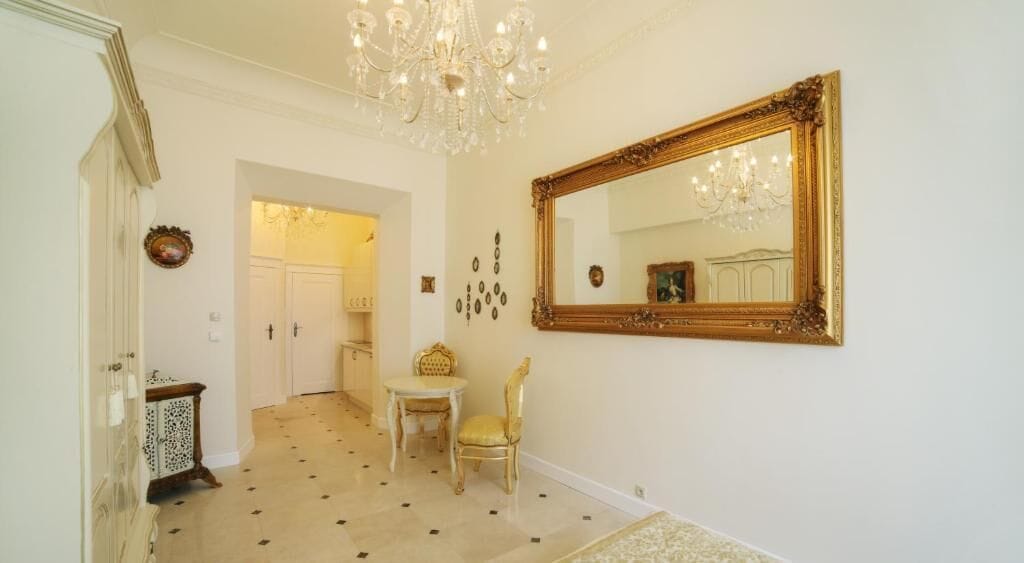 A hallway with a chandelier, a large mirror, a chair, and a door leading to another room.
