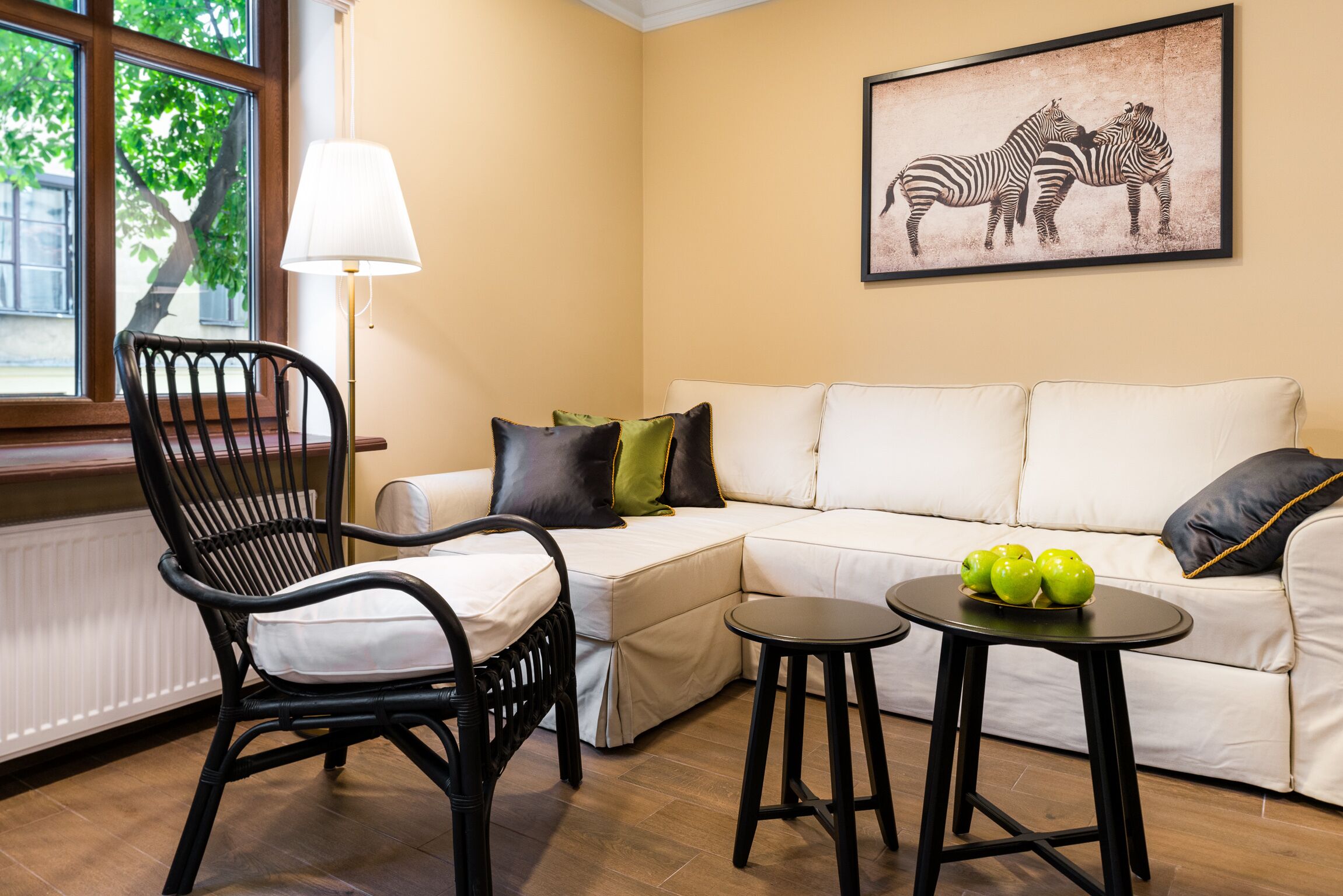 Ein Wohnzimmer mit einem schwarzen Korbstuhl, einem weißen Sofa, einem kleinen runden Tisch mit grünen Äpfeln und einem Zebra-Gemälde an der Wand.