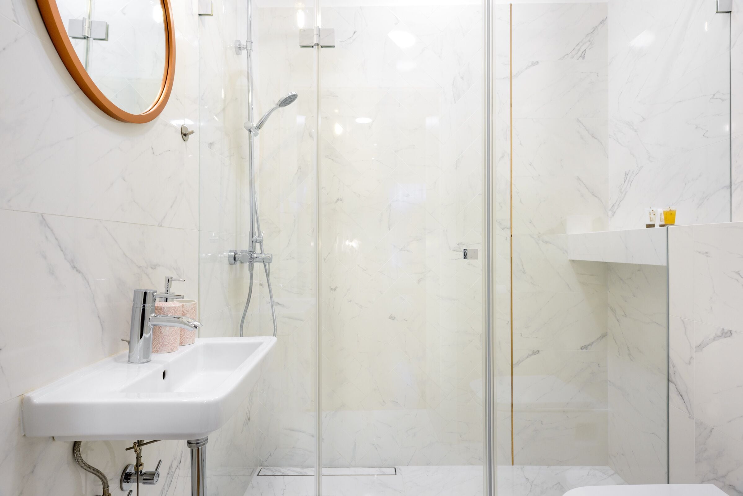 Un baño moderno con lavamanos blanco, cabina de ducha de cristal y paredes de mármol.