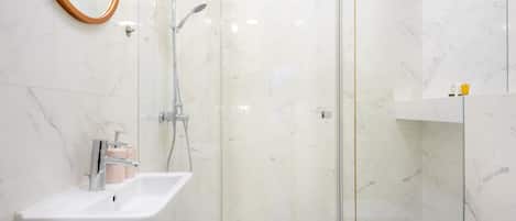 Un baño moderno con lavamanos blanco, cabina de ducha de cristal y paredes de mármol.