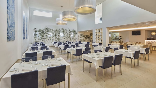 A spacious dining area with multiple tables, chairs, and hanging pendant lights.