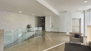 A modern interior with a glass railing, a staircase, a reception desk, and a sofa.