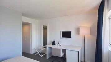 A hotel room with a bed, a desk with a TV, a lamp, and a clothes drying rack.