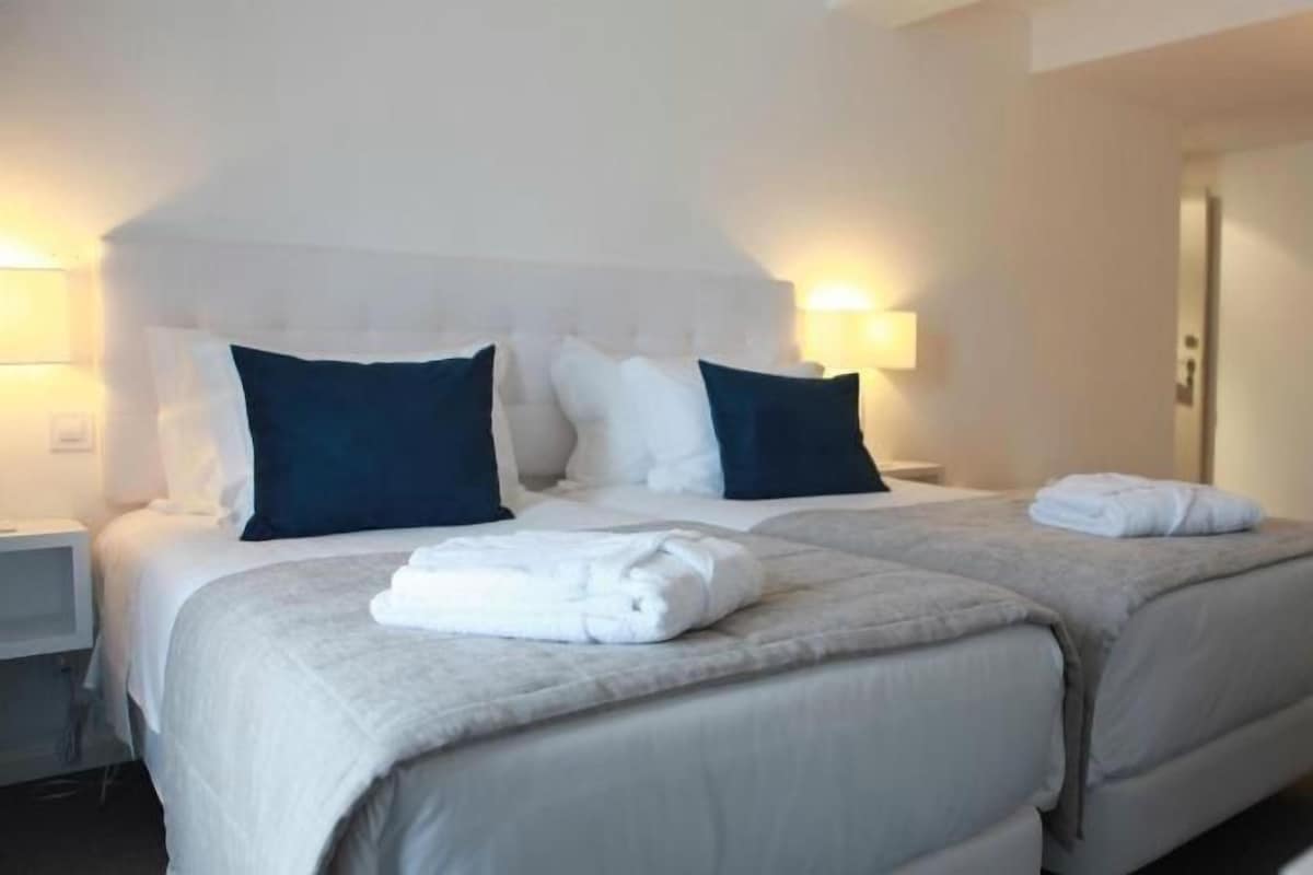A hotel room with two beds, a nightstand, a lamp, and a chair.