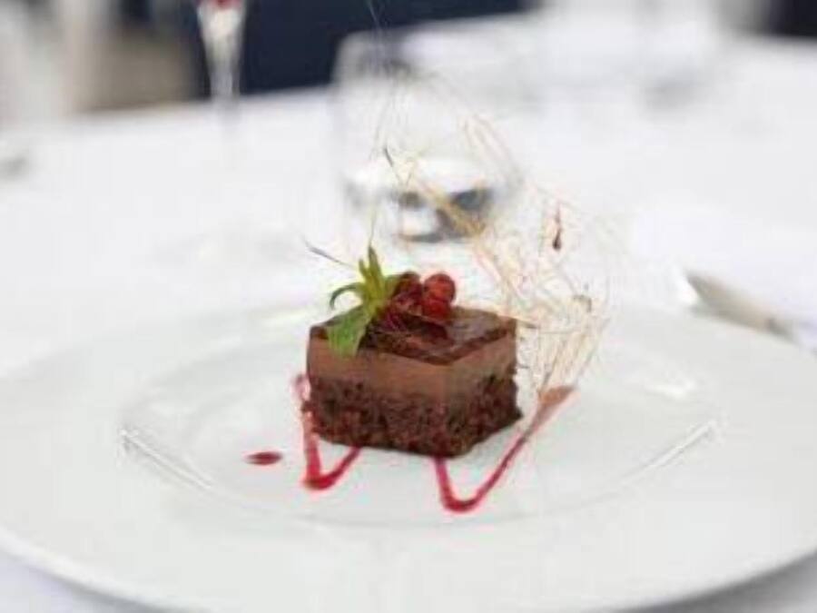 Un postre sobre un plato blanco, con una cúpula de cristal transparente y salsa roja.