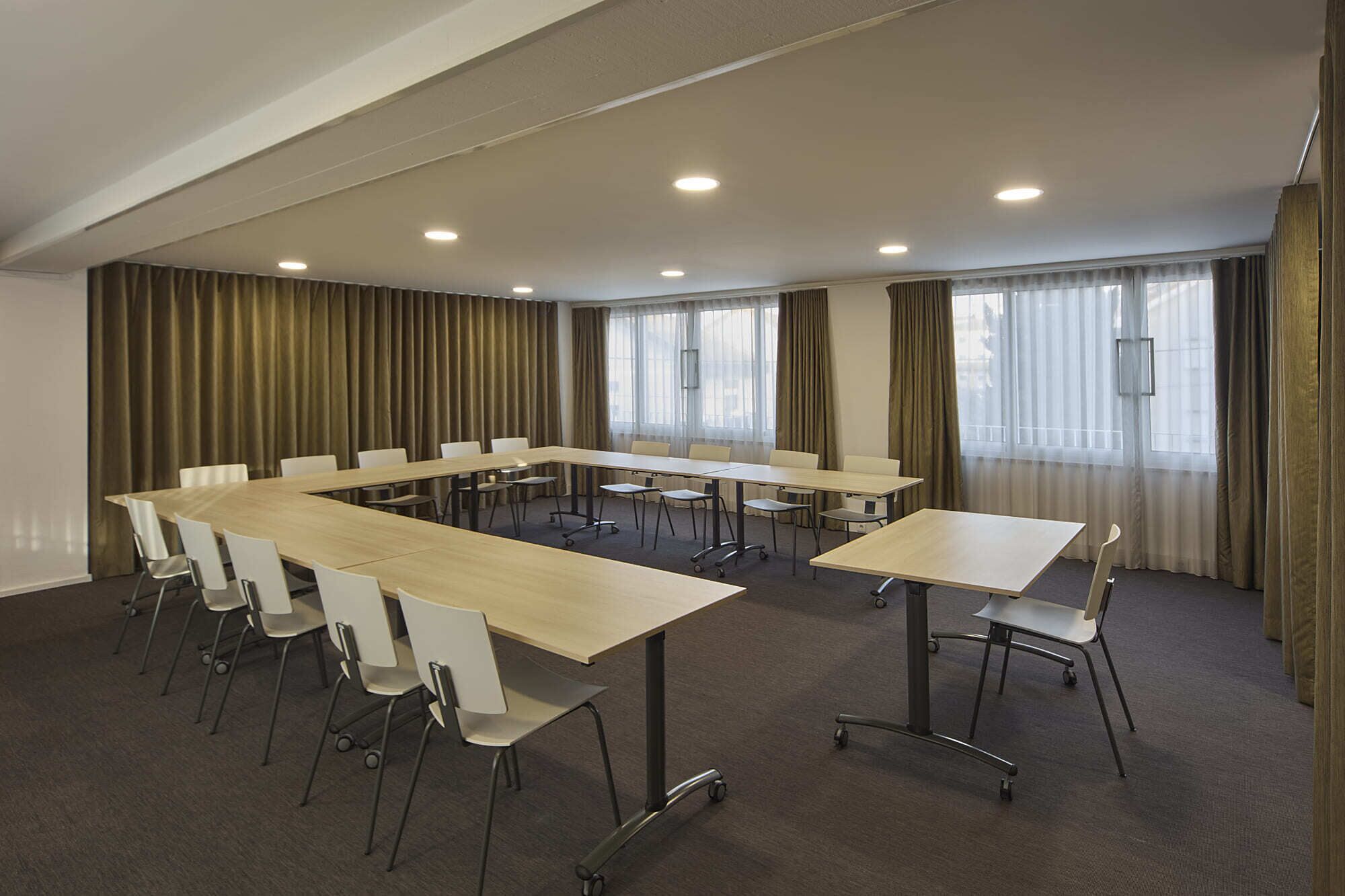 Ein Konferenzraum mit einem langen Tisch, weißen Stühlen und einem Teppichboden.