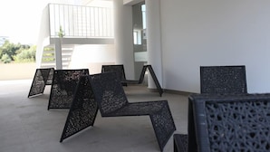 A modern interior with black woven chairs arranged in a semi-circle, a staircase, and a large window providing a view of greenery outside.