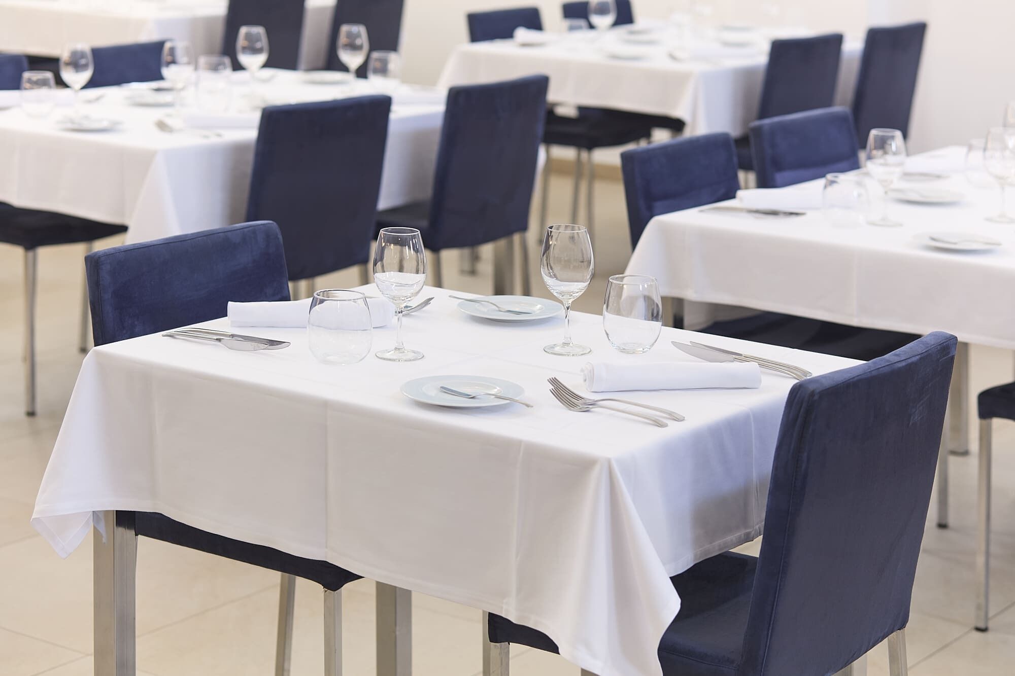 A dining area with tables set for service, chairs, and dining ware.