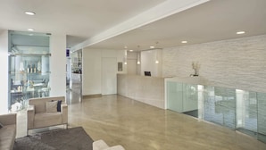 A spacious, modern interior with a glass railing, a reception desk, and a seating area with a sofa and armchairs.