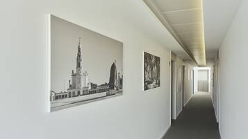 A hallway with a long corridor, a large framed picture on the left wall, and a smaller framed picture on the right wall.