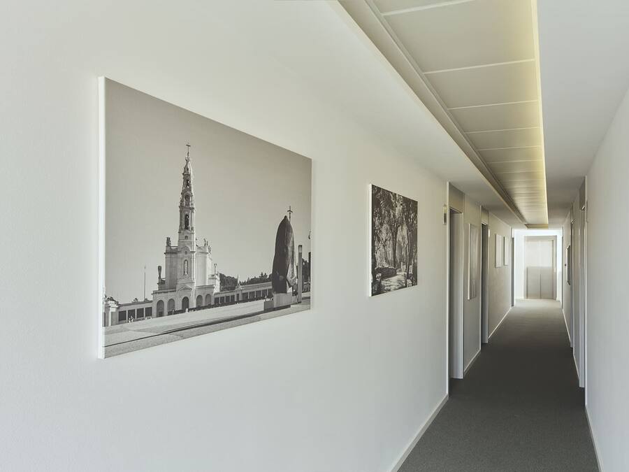 A hallway with a long corridor, a large framed picture on the left wall, and a smaller framed picture on the right wall.