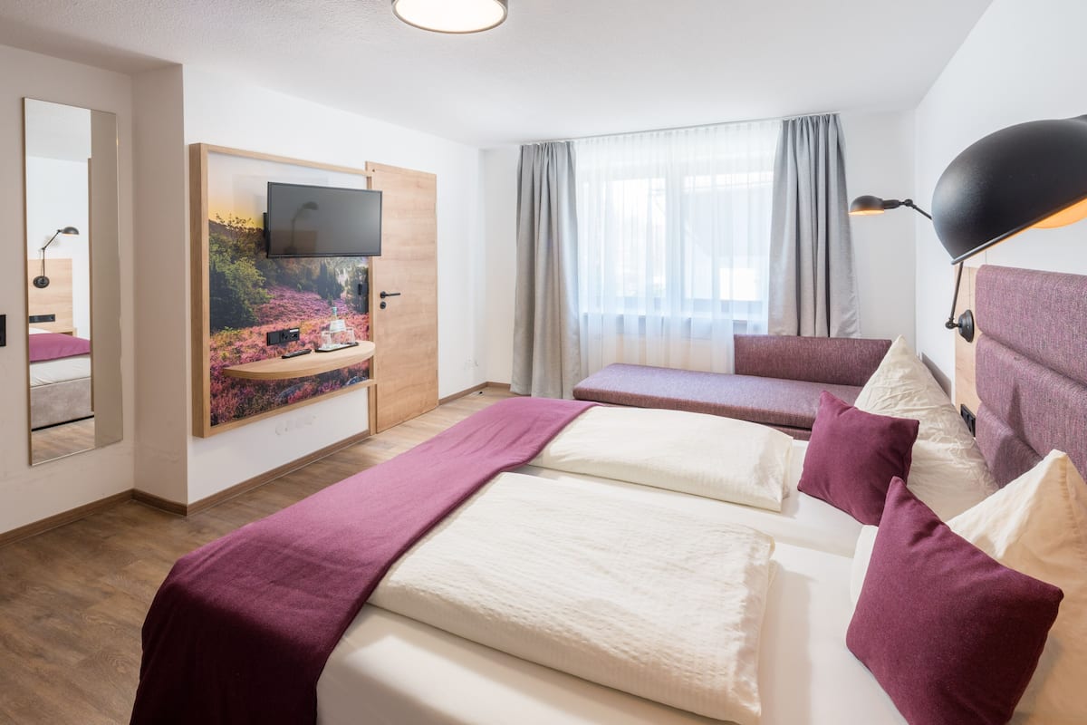 A hotel room with two beds, a TV, a large window with curtains, and a mirror.