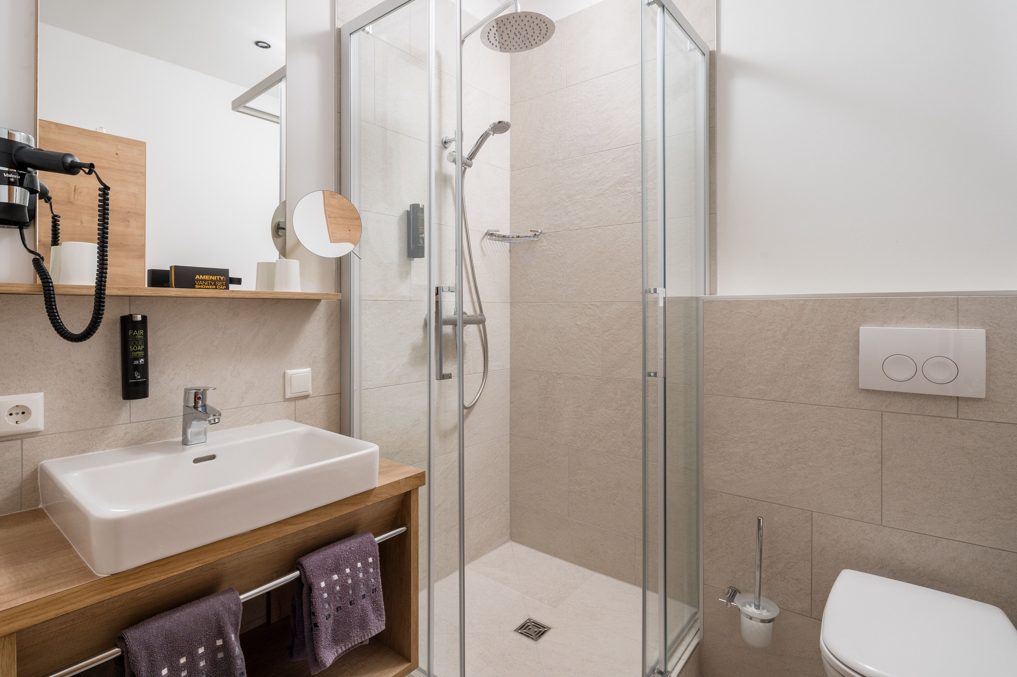 Une salle de bain moderne avec une douche à parois de verre, un lavabo doté d’un plan de toilette en bois et des toilettes.
