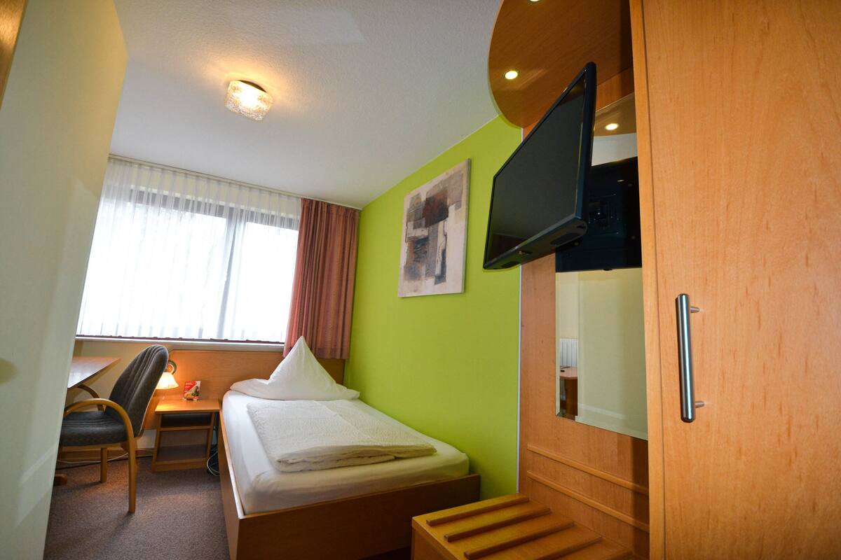 A hotel room with a bed, a desk, a chair, a television, and a window with curtains.