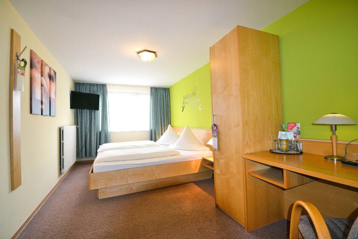 A hotel room with a bed, a desk, a chair, a TV, and a window with curtains.