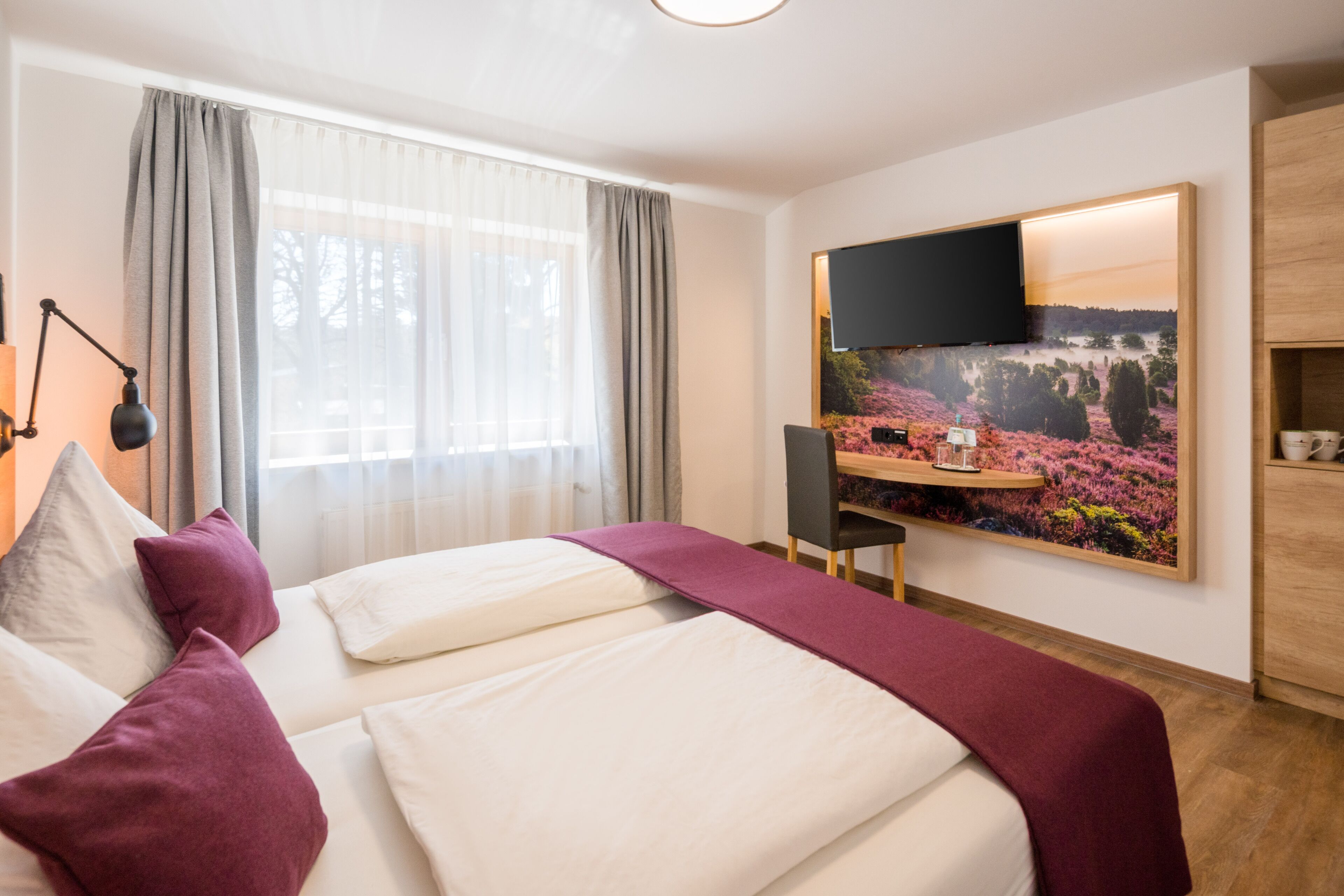 A hotel room with a bed, a desk, a chair, a TV, and a painting on the wall.