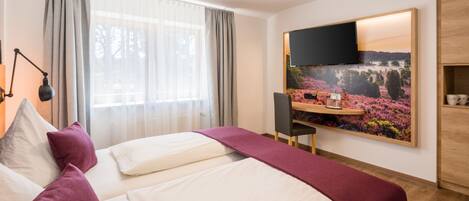 A hotel room with a bed, a desk, a chair, a TV, and a painting on the wall.