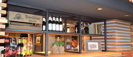 Una zona de bar con estantes llenos de botellas y vasos, una barra de madera y un cuadro enmarcado.