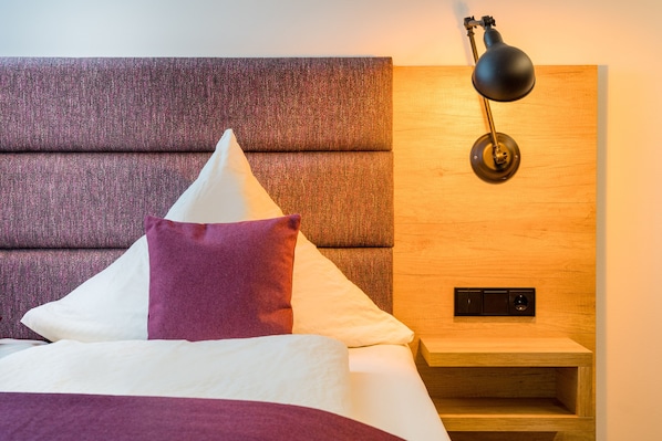 A neatly made bed with a headboard, pillows, and a bedside table with a lamp. - Heidehotel Bockelmann (Bispingen)