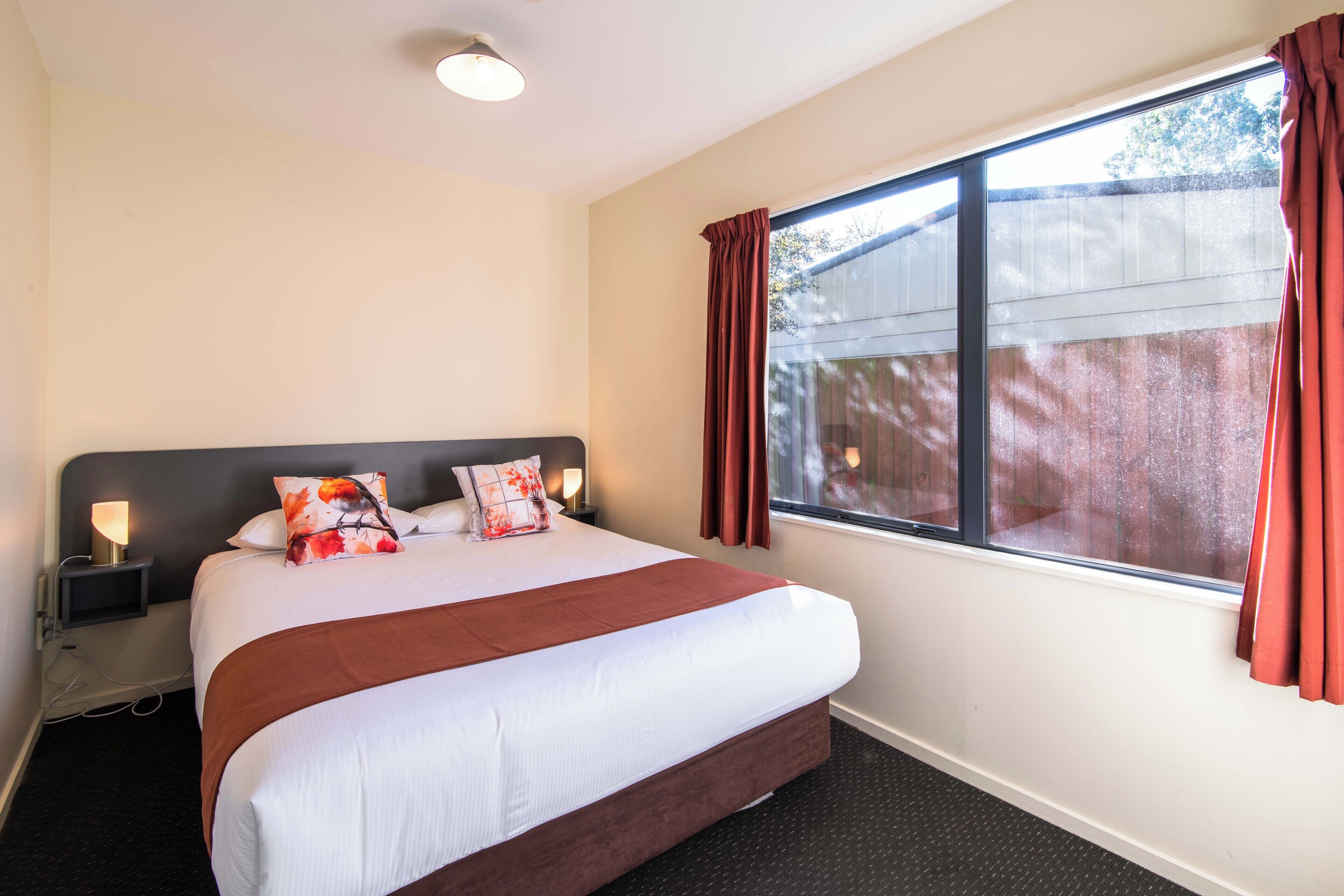Habitación de hotel con una cama grande, una mesita de noche con lámpara, una ventana con cortinas y vistas al exterior.