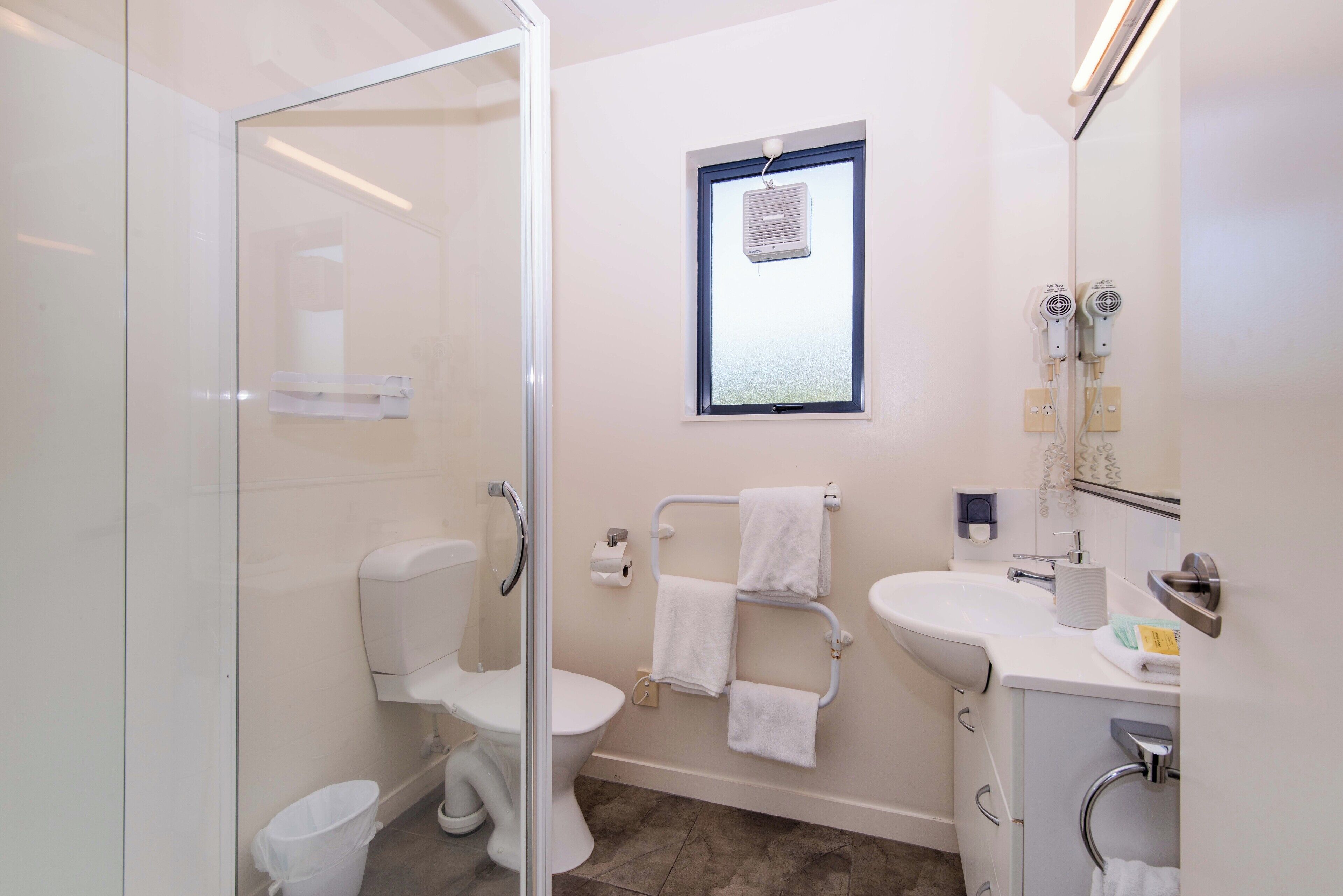 A modern bathroom with a glass shower enclosure, a toilet, a sink, and a mirror.