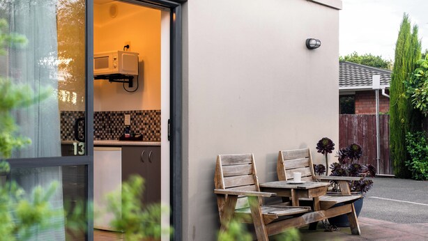 A modern kitchen with a microwave, a small refrigerator, and a tiled backsplash. There is a wooden table and chairs outside the kitchen, with a potted plant nearby. - 298 Westside Motor Lodge (Christchurch)