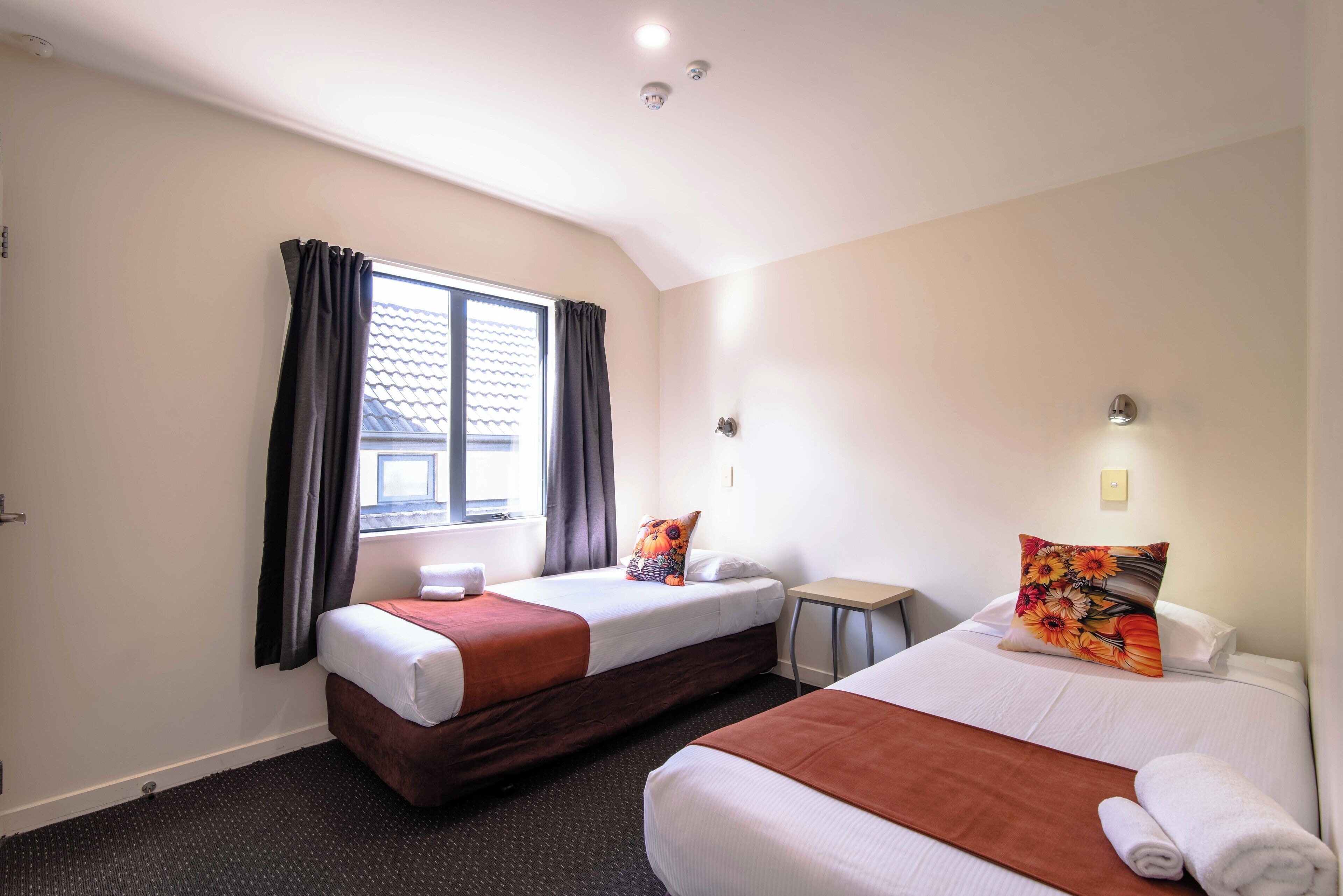 Een hotelkamer met twee bedden, een raam met gordijnen, een klein tafeltje en een wandlamp.