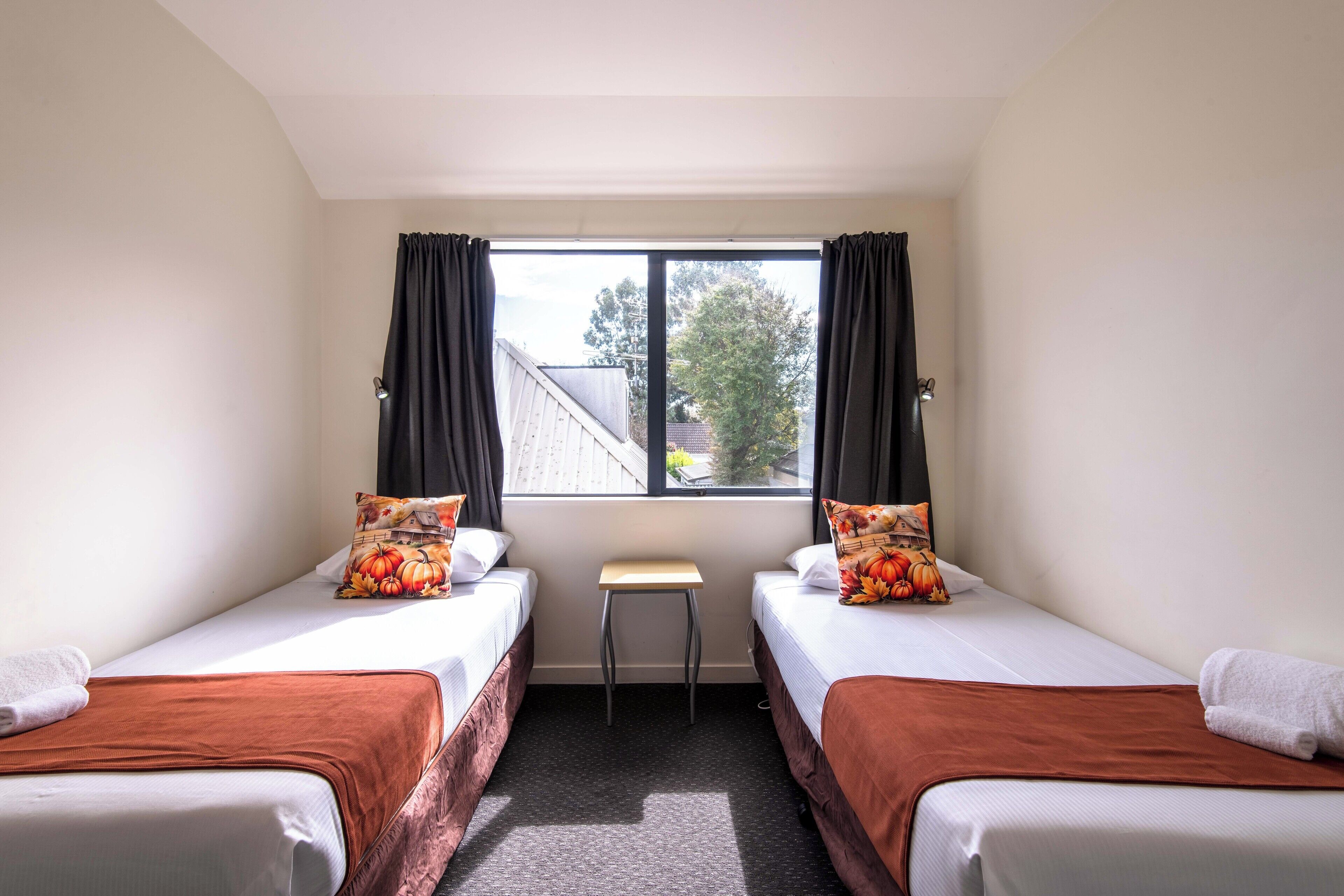 Une chambre avec deux lits, une petite table et une fenêtre avec des rideaux.