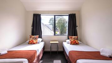 Une chambre avec deux lits, une petite table et une fenêtre avec des rideaux.