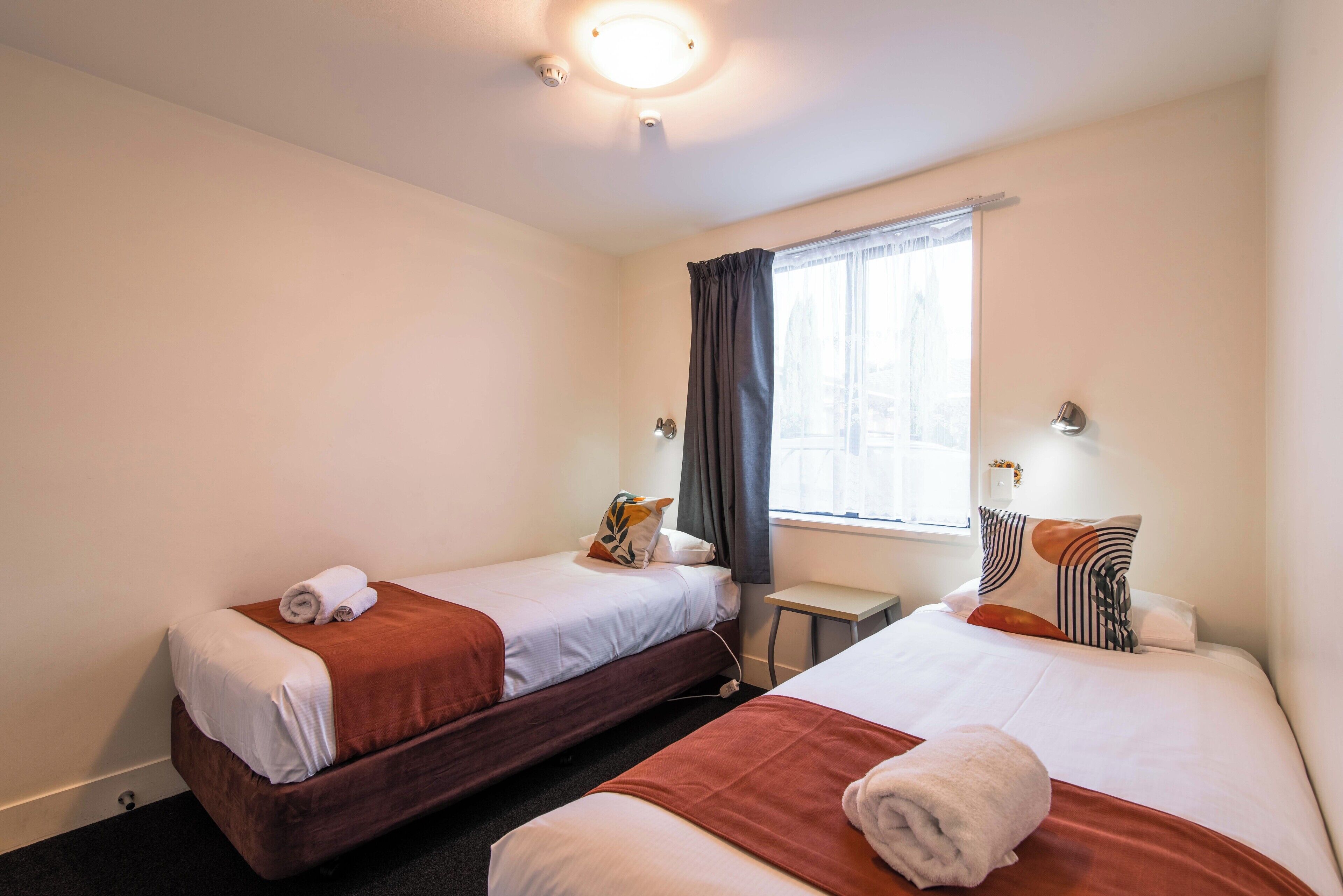 A hotel room with two beds, a small table, and a window with curtains.