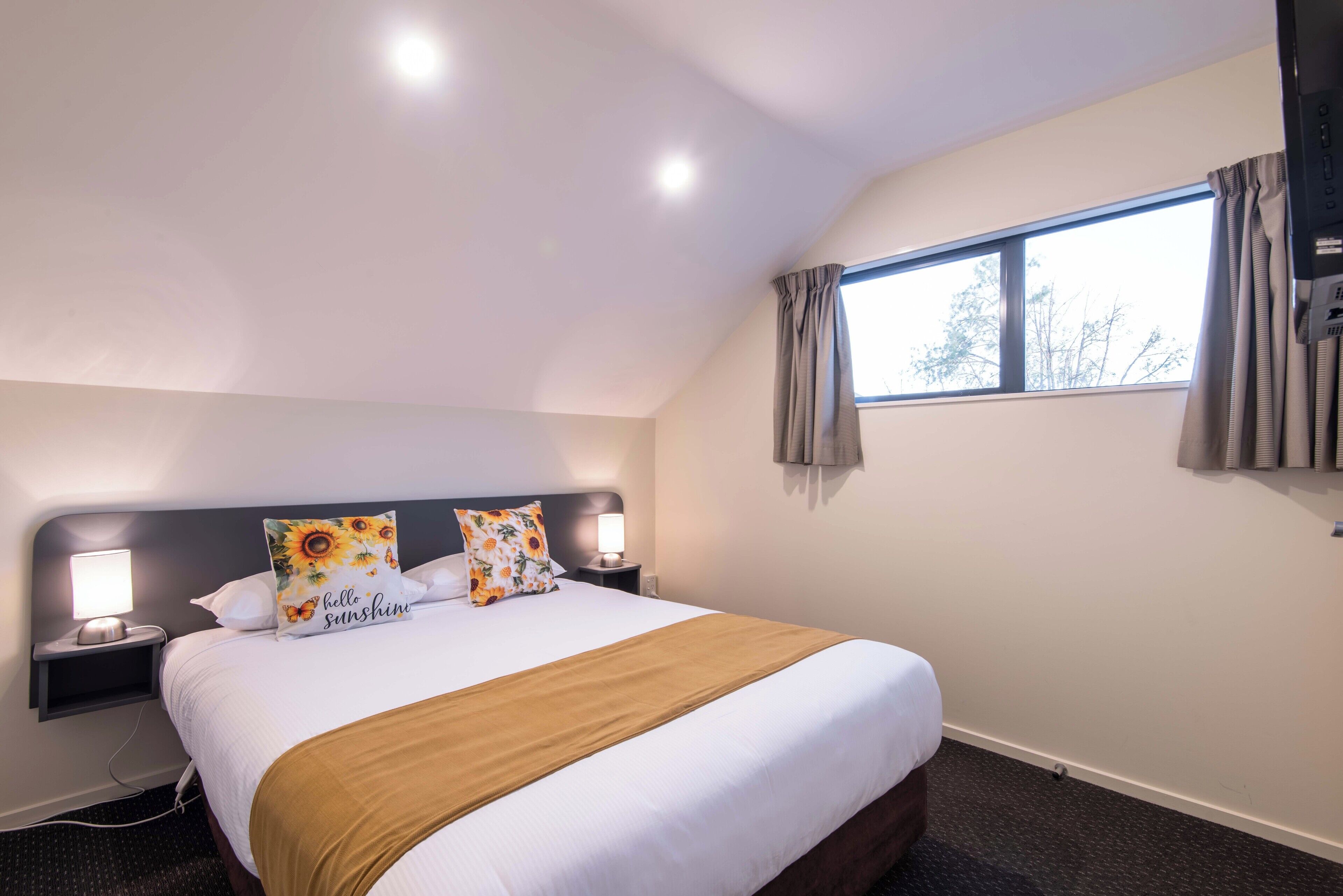 A hotel room with a large bed, two bedside lamps, a window with curtains, and a wall-mounted air conditioning unit.