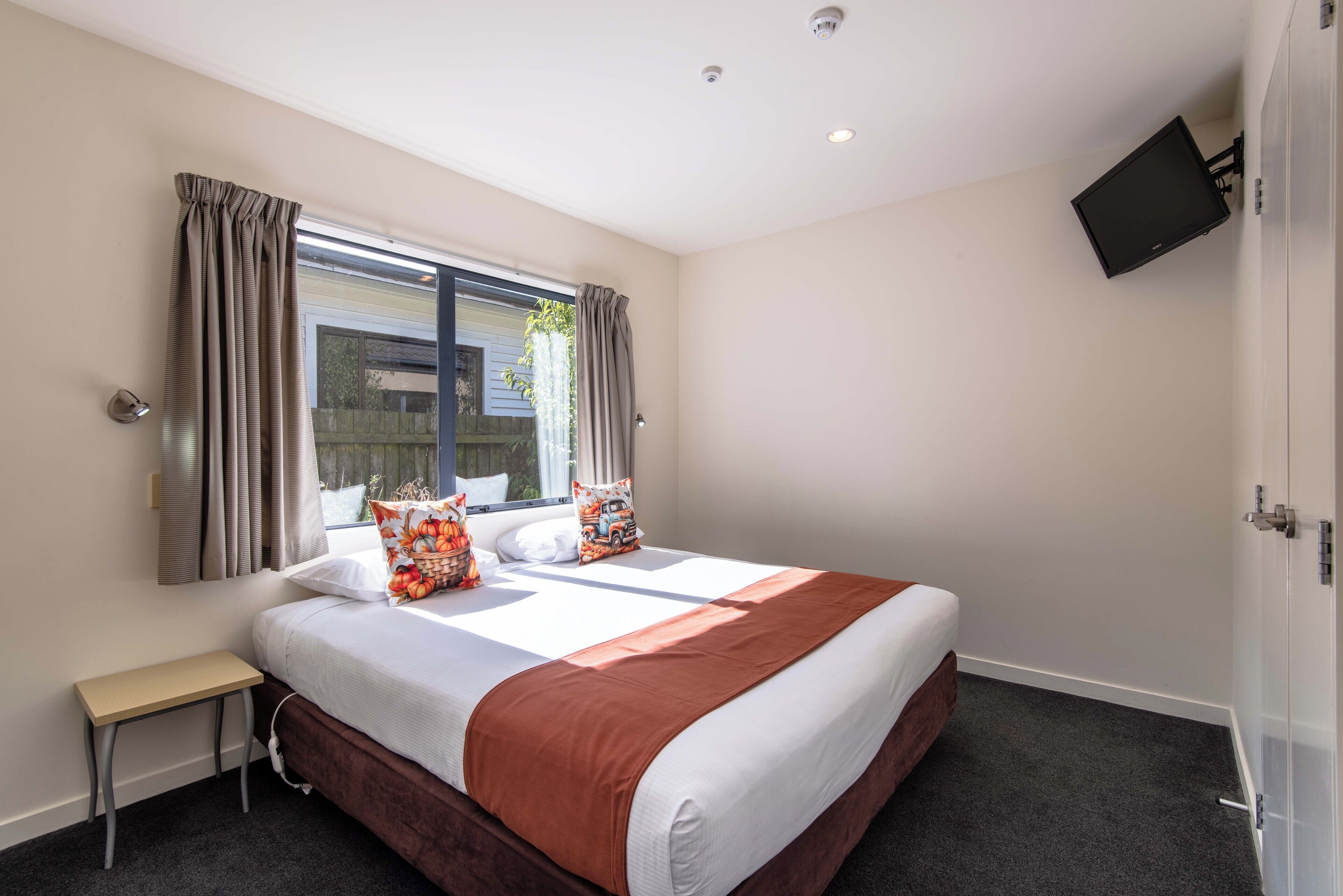 A hotel room with a large bed, a small bedside table, a window with curtains, and a mounted TV.